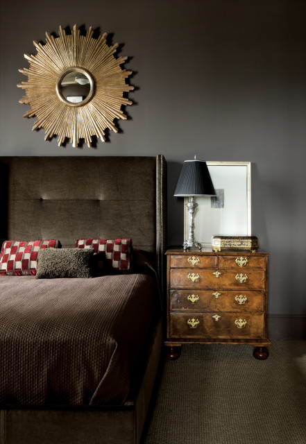 Bedroom with a tufted brown headboard, gold sunburst mirror, and a vintage wooden dresser with brass hardware.