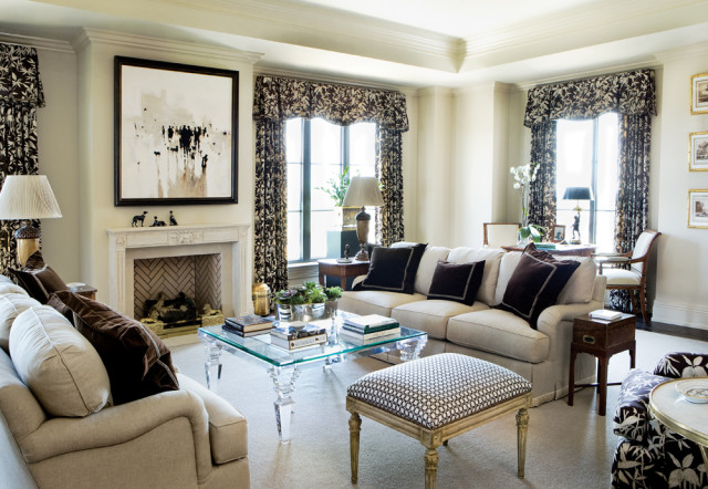 Living room with a neutral-toned sofa, dark patterned curtains, a glass coffee table, and a fireplace with abstract art above.