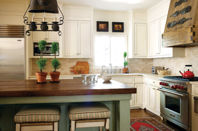 Cream kitchen with wood island, stainless steel appliances, stone tile backsplash, and wrought iron chandelier