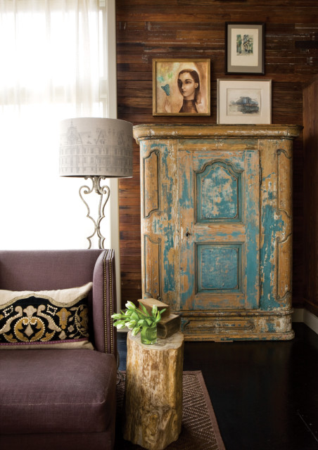 Living room corner with a purple upholstered armchair, a distressed turquoise armoire, and a wood stump side table with books and tulips.