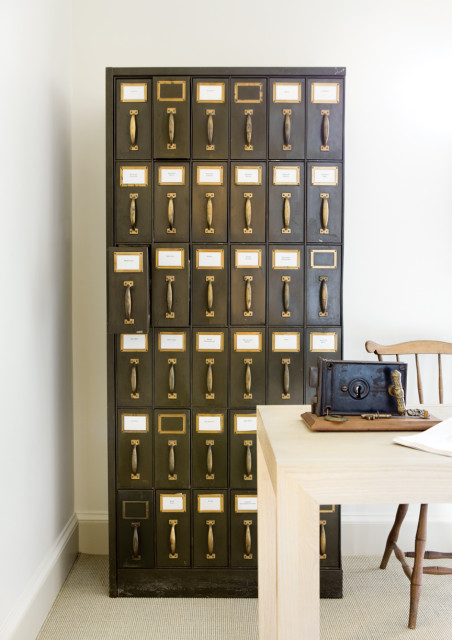 Dark green filing cabinet with brass hardware and wooden handles, next to a light wood desk with an antique lockbox and keys.