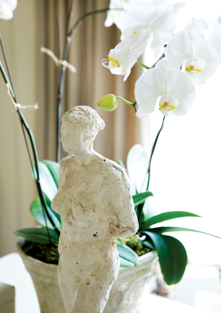 A textured, off-white plaster sculpture of a torso stands in front of white orchids and green orchid leaves in a distressed pot.