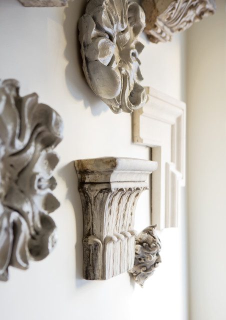 Close-up of ornate, carved plaster architectural details in shades of white and grey mounted on a white wall.