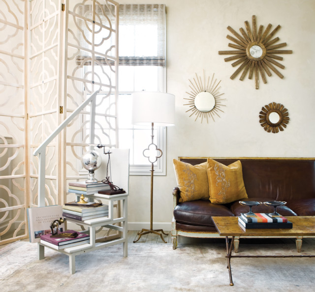 Living room with a brown leather sofa, gold sunburst mirrors on the wall, a white decorative screen, and a step-style bookshelf filled with books.