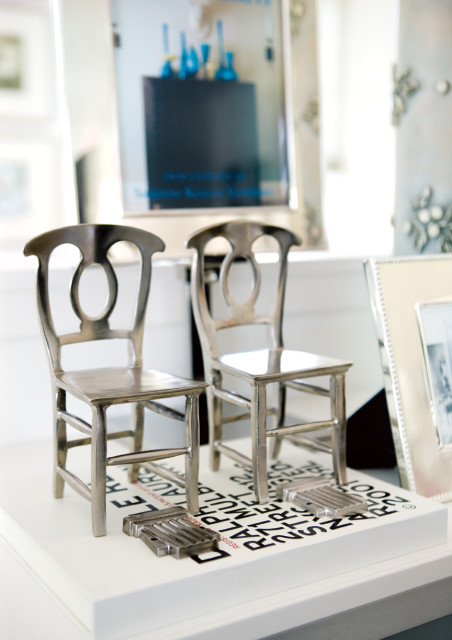 Two miniature silver chairs with oval back cutouts displayed on a white surface with black text and two small metal objects in front.