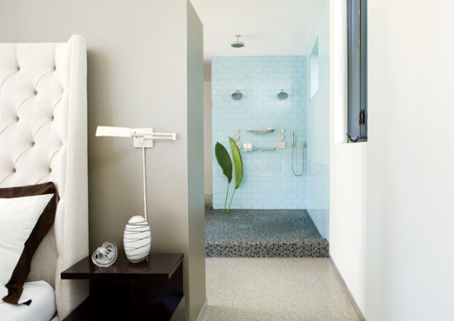 Bedroom with tufted headboard and bedside table next to a walk-in shower with light blue tile and pebble floor