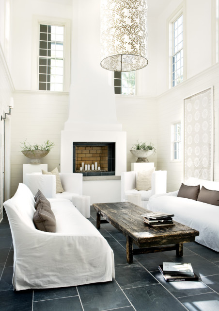 Spacious living room with white slipcovered sofas, a large white fireplace, a rustic wooden coffee table, and a tall drum pendant light with a leaf pattern.