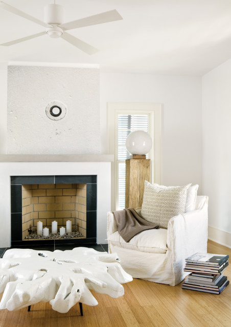 Living room with white slipcovered armchair, stacked books, white root coffee table, and fireplace with white candles.