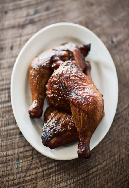 Close-up of roasted chicken quarters on a white plate, with a dark wood background.