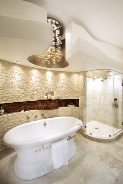 Luxurious bathroom with a freestanding white soaking tub, stone accent wall, glass-enclosed shower with marble tile, and a unique bubble chandelier