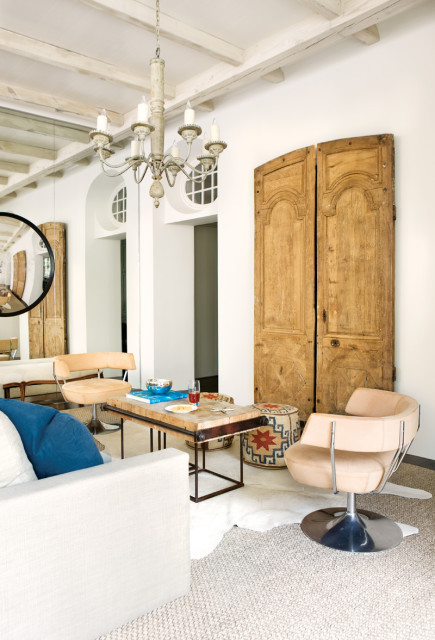 Living room with white sectional sofa, tan swivel chairs, rustic wood coffee table, and antique double doors on white wall.