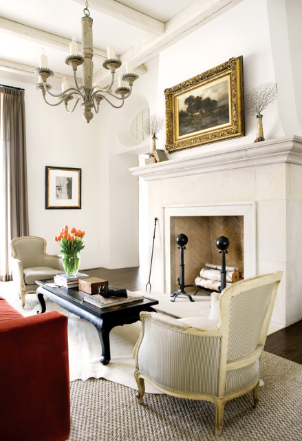 Living room with a large stone fireplace, ornate chandelier, and antique-style chairs. A black coffee table holds a vase of orange tulips.