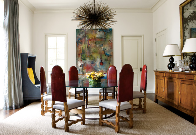 Dining room with a glass-top table surrounded by six red leather chairs, a large abstract painting, and a sputnik chandelier.