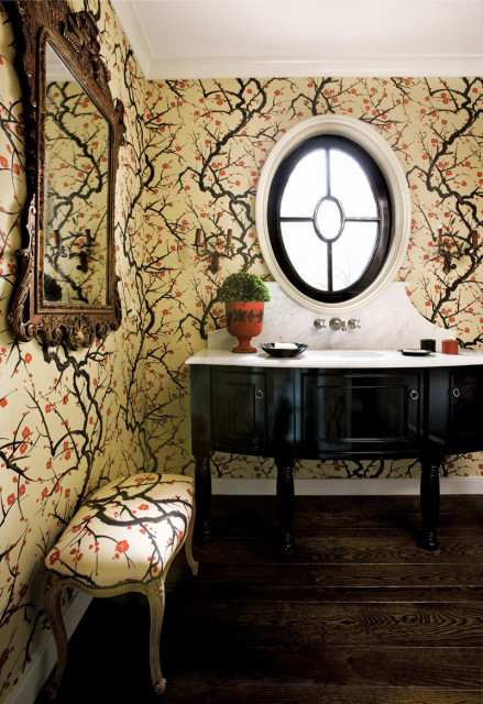 Powder room with bold floral wallpaper, a black vanity with a marble countertop, an oval window, and a vintage bench.