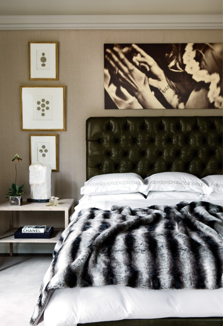 Bedroom with a dark green tufted leather headboard, crisp white bedding, and a plush faux fur throw. Three framed botanical prints hang above the headboard, alongside a large black and white artwork.