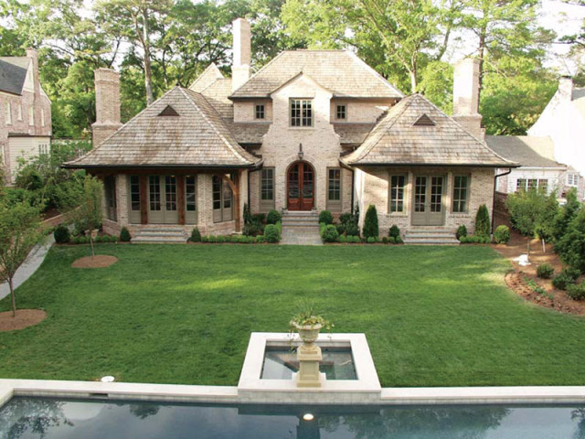 French-inspired brick residence with multi-gabled cedar shake roof, large manicured lawn, and swimming pool.