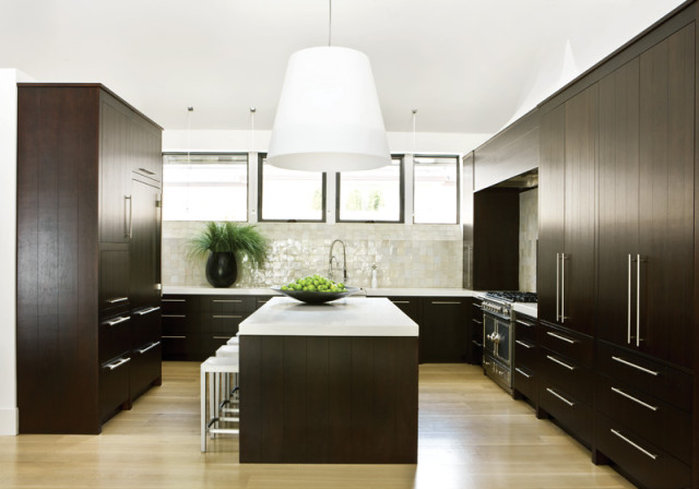 Dark wood kitchen with white quartz island, stainless steel appliances, and a textured tile backsplash.