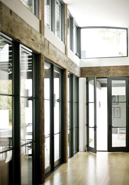 Modern interior with large glass doors and windows, exposed wooden beams, and light wood floors.