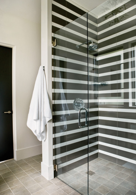 Modern bathroom with a glass-enclosed shower featuring black and white horizontal striped tile, chrome fixtures, and a white towel hanging on a nearby hook.