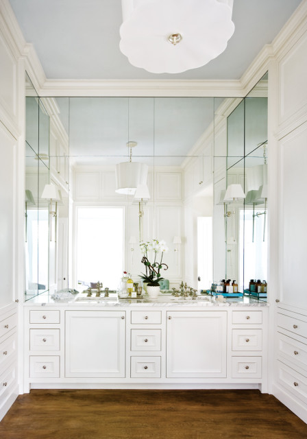 White bathroom with double vanity, marble countertop, mirrored wall, and built-in cabinetry.