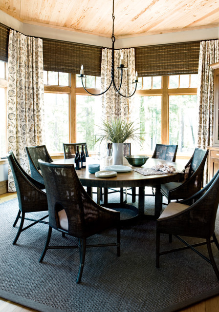 Round dining table with dark woven chairs, set with plates and wine bottles, under a wrought iron chandelier and wood plank ceiling.