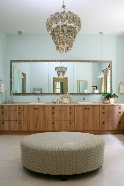 Clean-lined cabinetry from Spain provides plenty of storage with more hidden behind a wall of mirrors. A custom ottoman and chandelier overhead lend an air of elegance while a spacious shower lined with sparkling glass tiles contributes to the ambience.