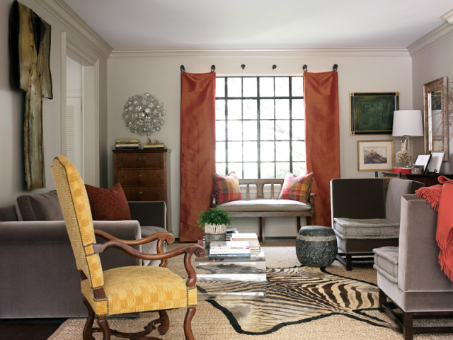 Living room with a yellow upholstered armchair, gray sofas, a zebra rug, and rust-colored curtains framing a window with a bench seat.