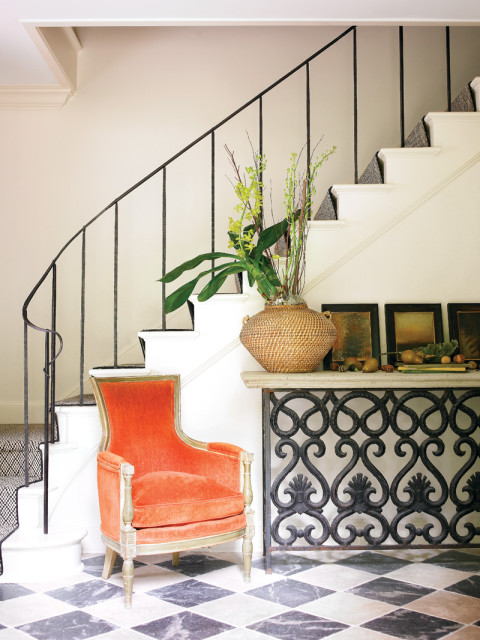 Entryway with a coral velvet armchair, a console table with a woven basket of greenery, and a black wrought iron railing along the staircase.