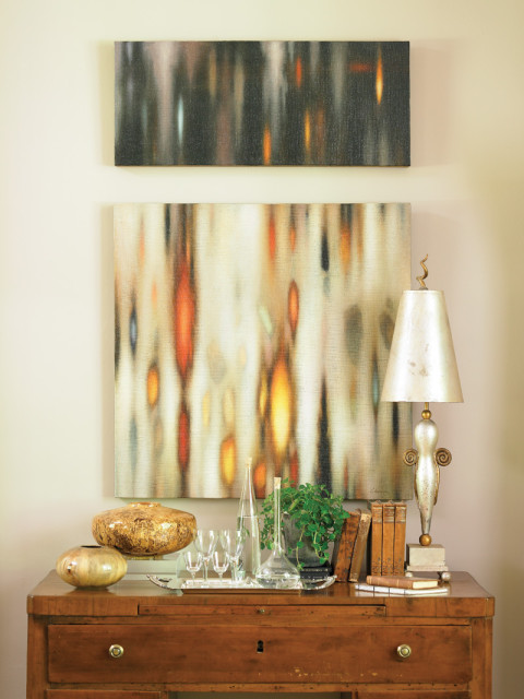 Wooden dresser topped with abstract art, decorative vases, glassware, books, and a metallic lamp.