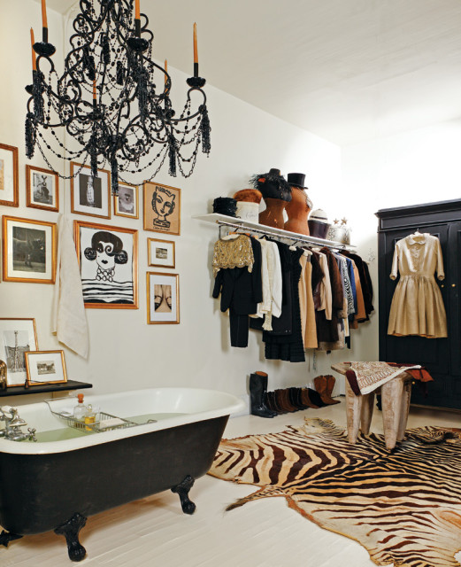Black clawfoot bathtub in a room with a black beaded chandelier, gallery wall of framed art, open clothing rack, and zebra print rug.