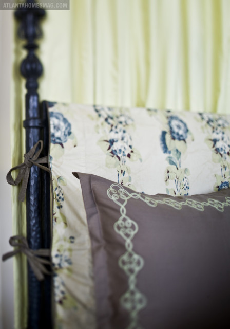Close-up of a dark-colored bed frame with floral patterned bedding and a taupe pillow with light green embroidery.