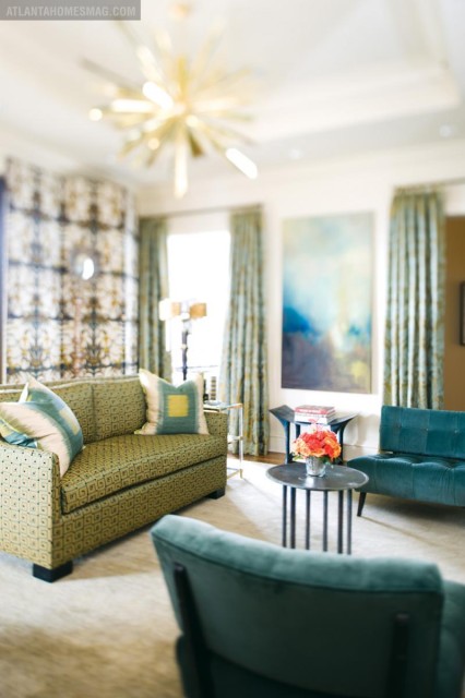Living room with a green patterned sofa, teal upholstered chairs, and a starburst chandelier. Blue and yellow abstract art hangs on the wall.