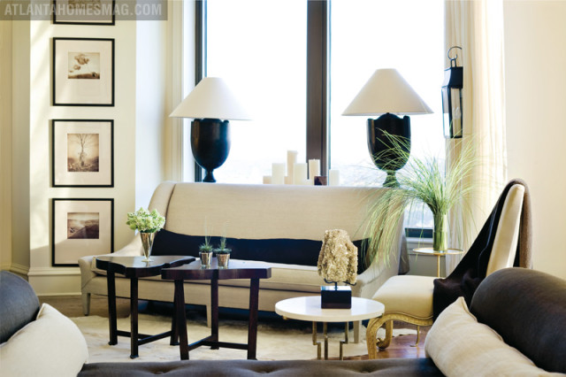 Living room with a neutral-toned sofa, dark wood side tables, and framed art on the wall. Two large lamps flank the sofa, with a vase of tall grass on a side table.
