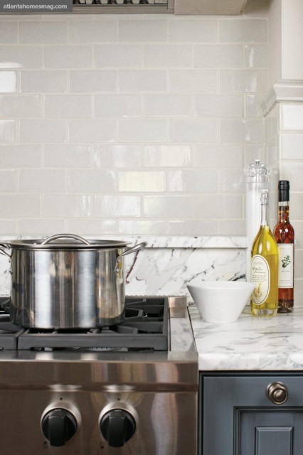 White subway tile backsplash in a kitchen with a stainless steel pot on a gas range and marble countertops.