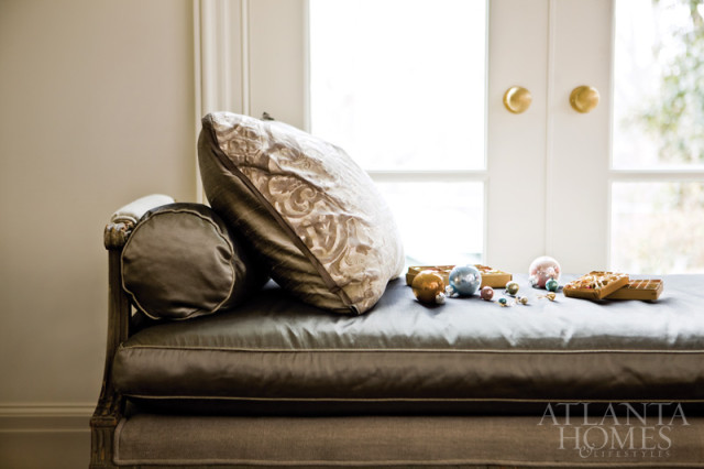 Chaise lounge with dark gray tufted cushions and decorative pillows, with Christmas ornaments and boxes on the seat.