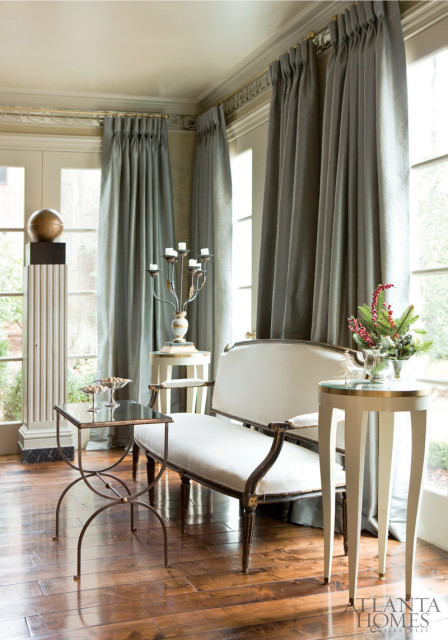 Living room with a white settee, dark wood floors, tall gray curtains, and decorative pedestal with a gold sphere.