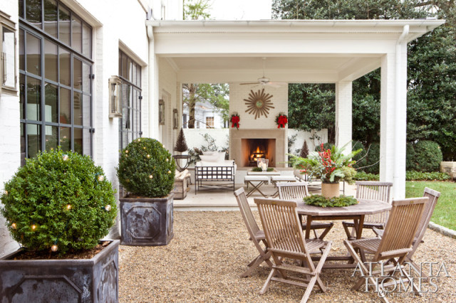 Covered patio with fireplace, outdoor dining set, and boxwood topiaries decorated with Christmas lights.