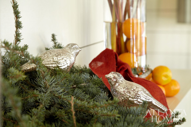 Two silver bird ornaments rest on a Christmas tree branch, with oranges and a red ribbon in the background.