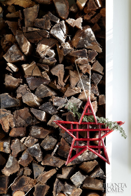 Red star ornament with evergreen sprigs hanging in front of a stack of chopped firewood.