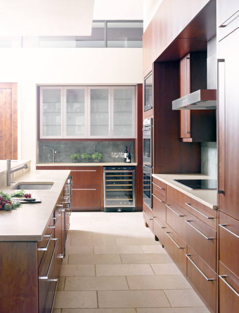 Modern kitchen with warm wood cabinetry, stainless steel appliances, wine fridge, and light stone tile flooring.