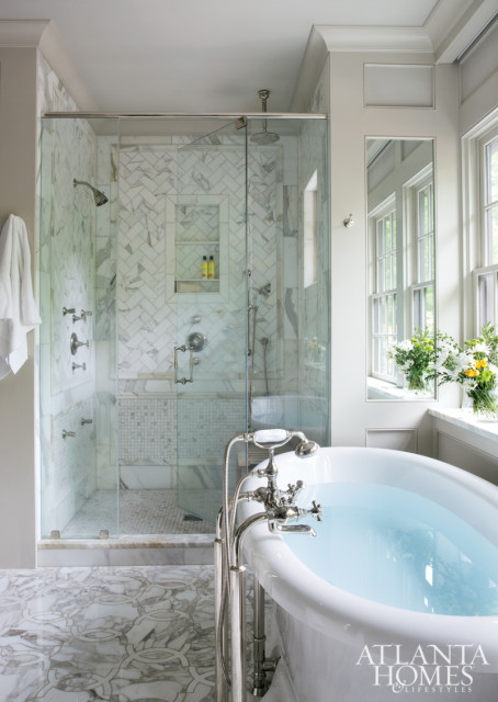 White bathroom with marble herringbone shower walls, freestanding soaking tub, and ornate marble floor.