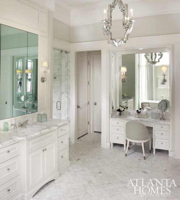 White bathroom with marble hexagonal floor, vanity with marble countertop, mirrored medicine cabinet, glass-enclosed shower, and a vanity table with a tufted stool.