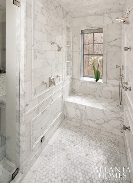 Marble tiled shower with hexagonal floor tiles, built-in bench, and a window overlooking trees. Features multiple shower heads and chrome fixtures.