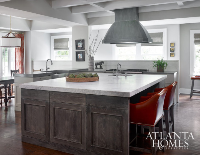 Kitchen island with dark wood cabinetry and marble countertop, featuring orange leather bar stools and a large metal range hood.