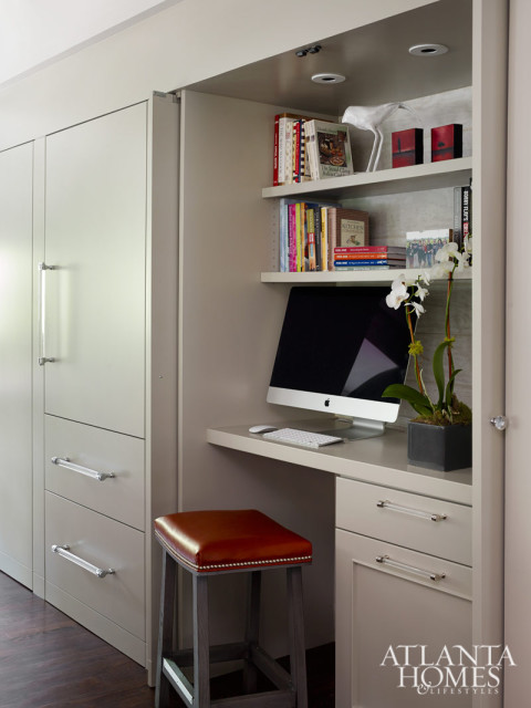 Built-in desk with a computer and shelves of books, next to a tall cabinet with clear drawer pulls. A brown leather stool sits in front of the desk.