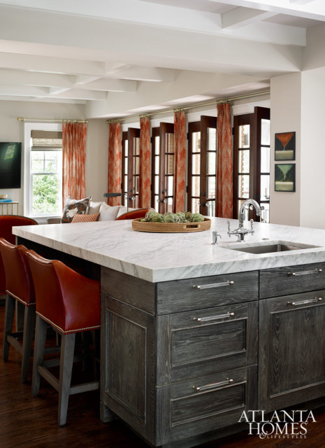 Kitchen island with white marble countertop, dark wood cabinetry, and red leather bar stools. A sink and faucet are visible on the countertop.
