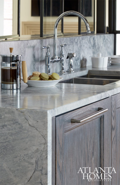 Kitchen counter with gray marble countertop, dark wood cabinetry, chrome faucet, French press, and macarons on a plate.
