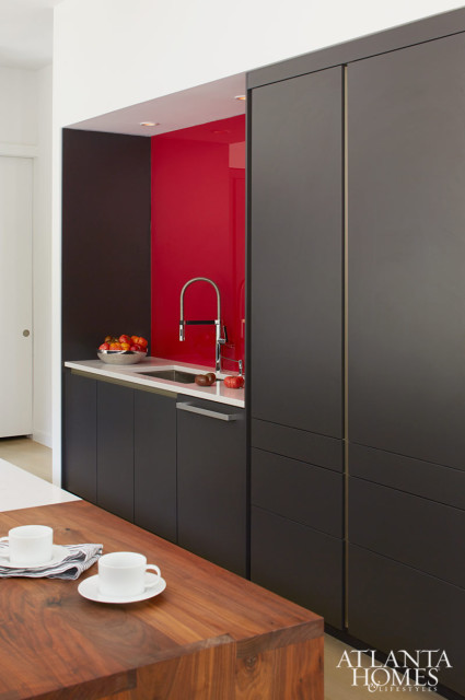 Modern kitchen with dark gray cabinetry, a white countertop, and a bright red backsplash. A stainless steel faucet is visible above the sink.