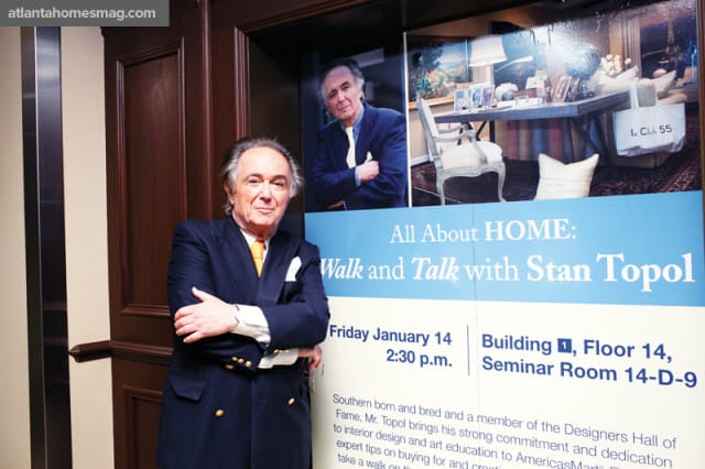 Stan Topol, wearing a navy blue suit and orange tie, stands with his arms crossed in front of a banner advertising "All About HOME: Walk and Talk with Stan Topol."