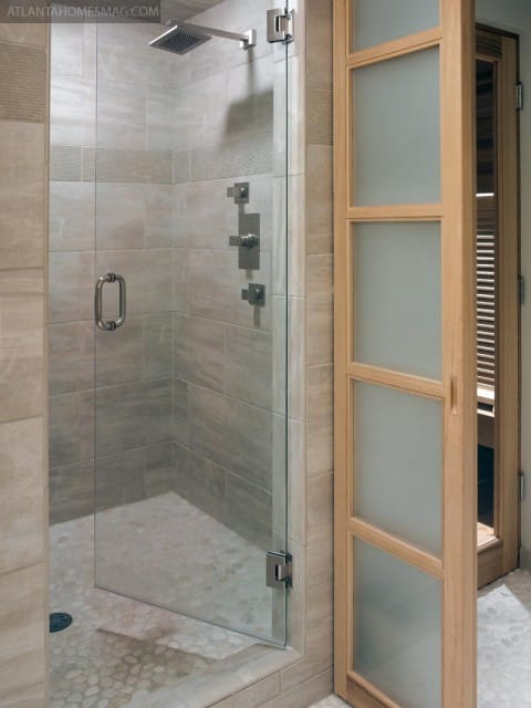 Shower with tiled walls, pebble floor, glass door, and wooden door with frosted glass panels.